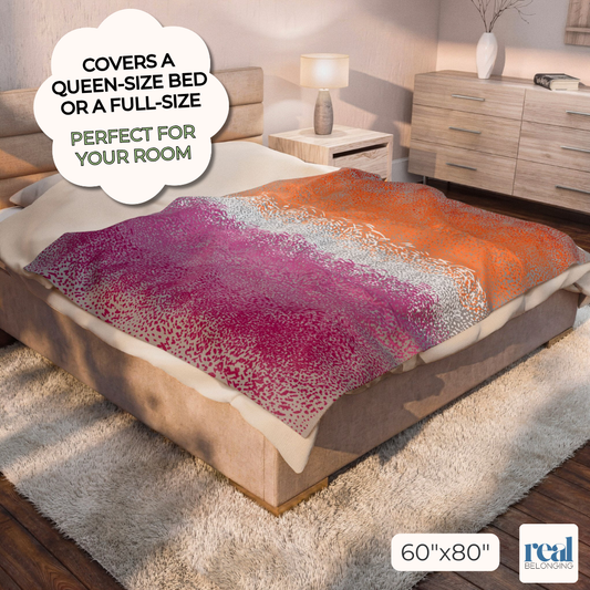 Lesbian Pride pink, white, and orange queen size blanket laid out on a king size bed in a neutral tan bedroom. Text reads: "Covers a queen-size bed or a full-size. Perfect for your room"