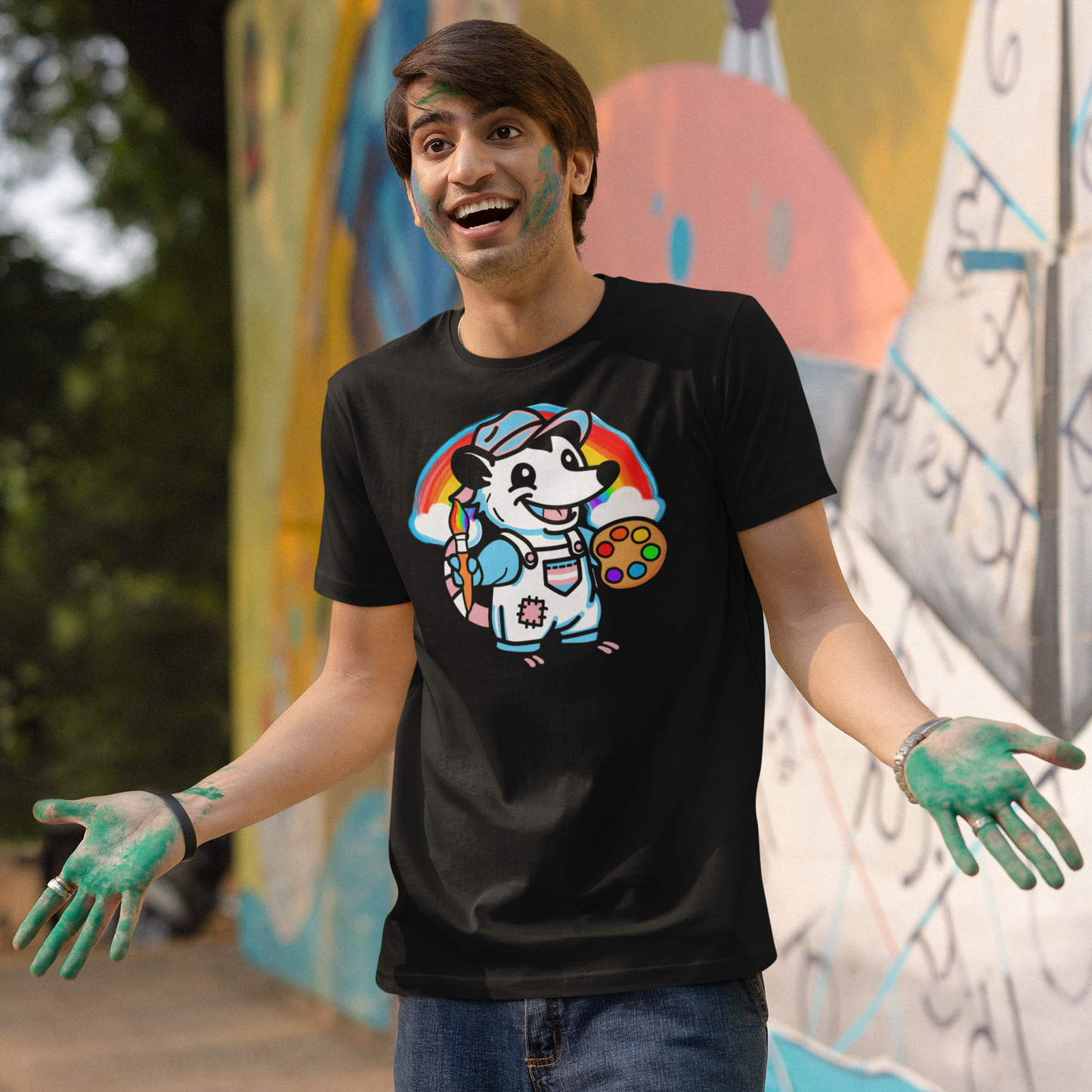 Person wearing a black t-shirt with a colorful graphic design, standing in front of a graffiti-covered wall.