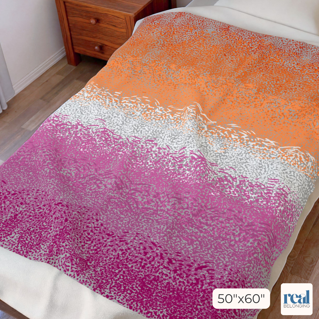 Gradient blanket transitioning from orange to pink on a bed with a wooden nightstand.