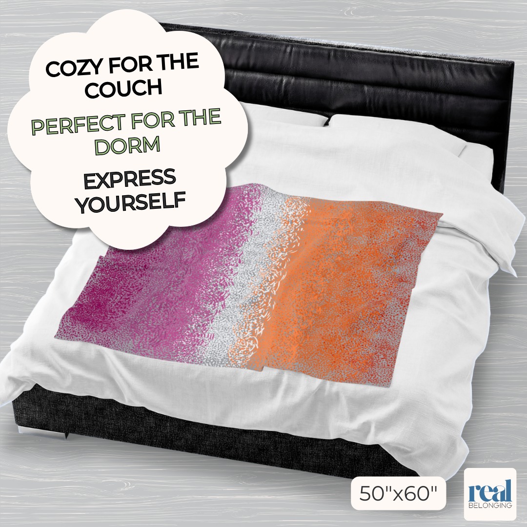 Colorful 50"x60" velveteen plush blanket with lesbian pride color spots dancing across a gray background, laid out on the middle of a king-size bed for perspective. Text reads: Cozy for the couch. Perfect for the dorm. Express yourself.
