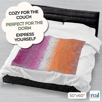 Colorful 50"x60" velveteen plush blanket with lesbian pride color spots dancing across a gray background, laid out on the middle of a king-size bed for perspective. Text reads: Cozy for the couch. Perfect for the dorm. Express yourself.